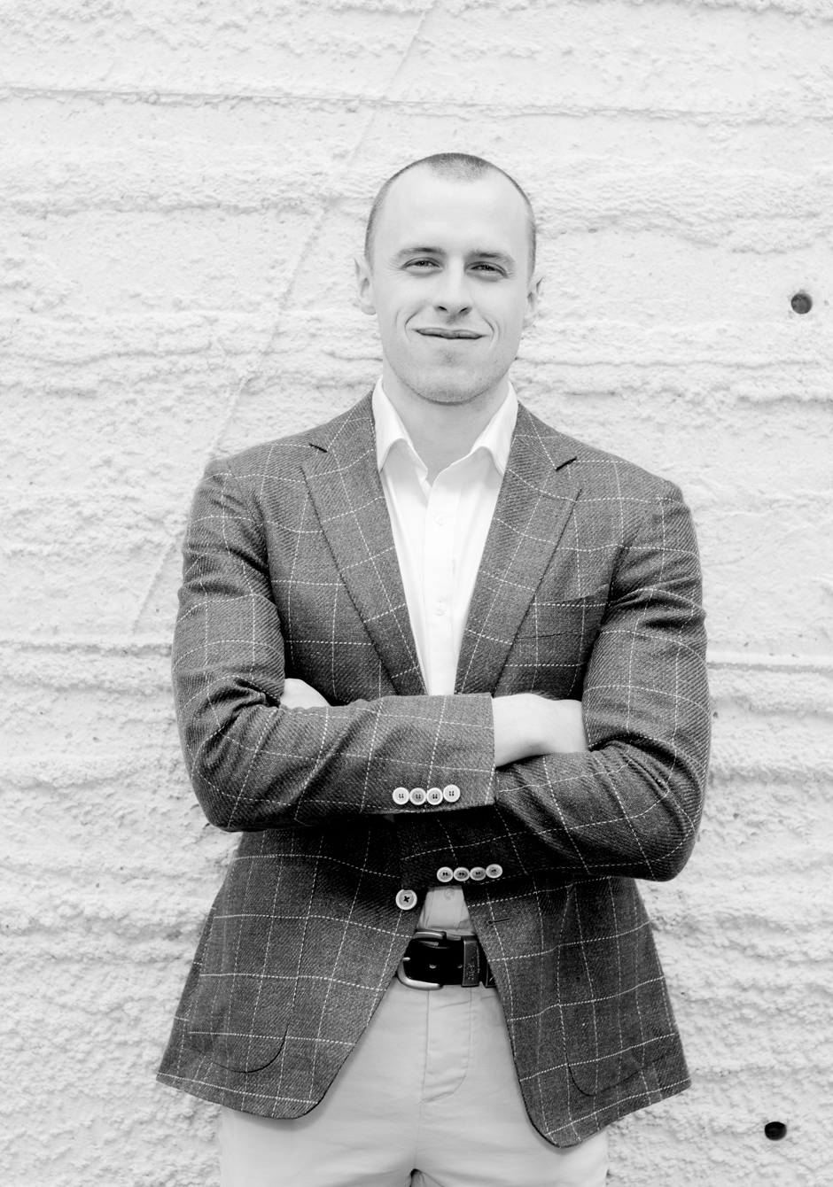 Black and white image of a man standing facing the camera. He is looking at the camera with his arms crossed.