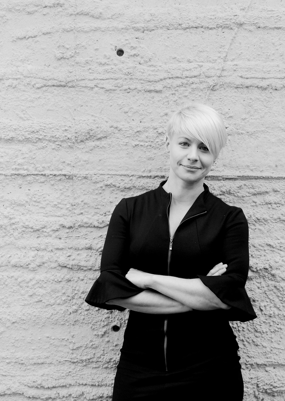 A black and white image of a woman smiling. She is facing the camera with her arms crossed.